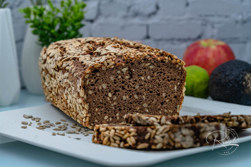 Dunkles Nordländer-Vollkornbrot mit Sonnenblumenkruste, angeschnitten auf einer weißen Platte
