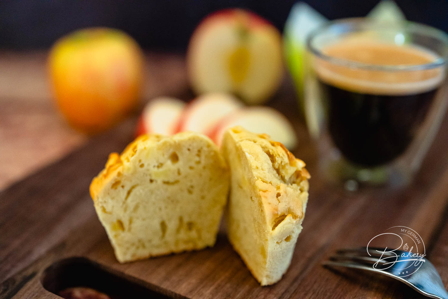 Halbierter Apfel-Muffin auf einem Holzbrett mit Äpfeln und Espresso im Hintergrund