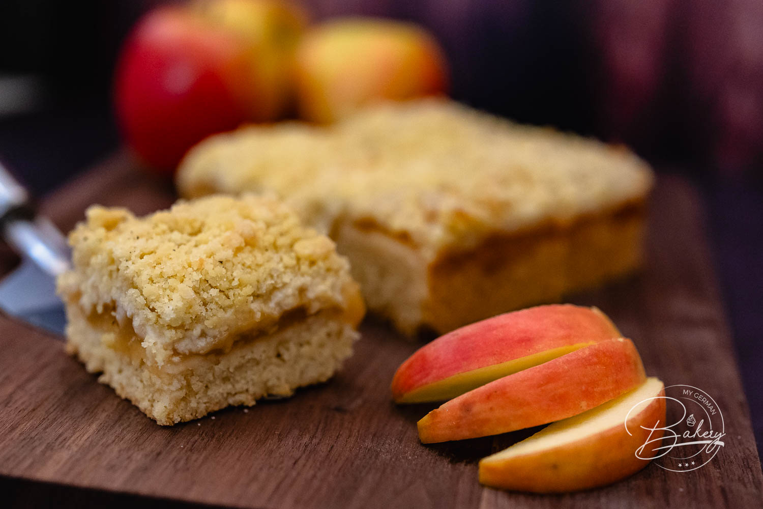 Apfelkuchen mit Streusel auf Holzbrett mit frischen Äpfeln und Apfelscheiben serviert