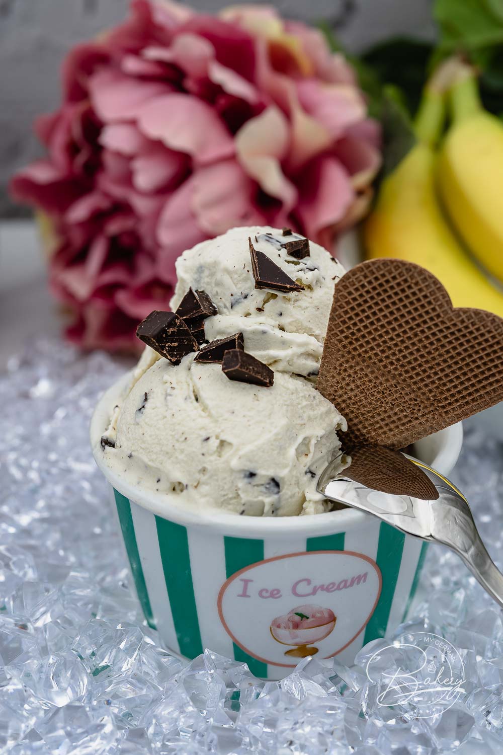 Cremiges Bananen-Split Eis mit dunkler Schokolade und Waffelherz im gestreiften Becher auf Eis