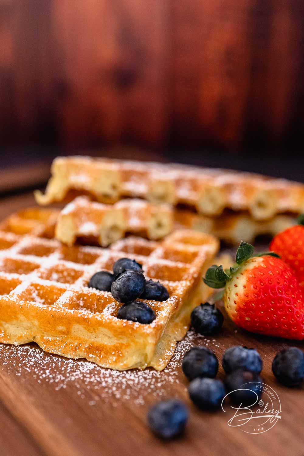 Frisch gebackene belgische Waffeln mit Puderzucker vor dunklem Holzhintergrund angerichtet