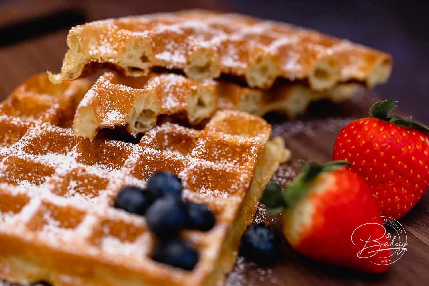 Gestapelte belgische Waffeln mit Puderzucker, frischen Blaubeeren und Erdbeeren auf einem Holzbrett