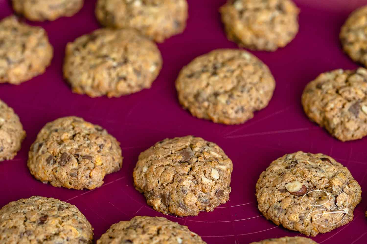 Fertig gebackene Cornflakes-Kekse mit Nüssen auf beerenroter Backmatte