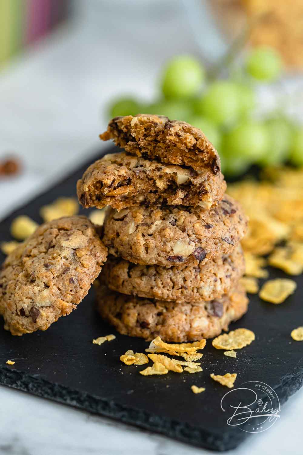 Knusprige Cornflakes-Kekse gestapelt auf Schieferplatte mit einzelnen Flakes davor