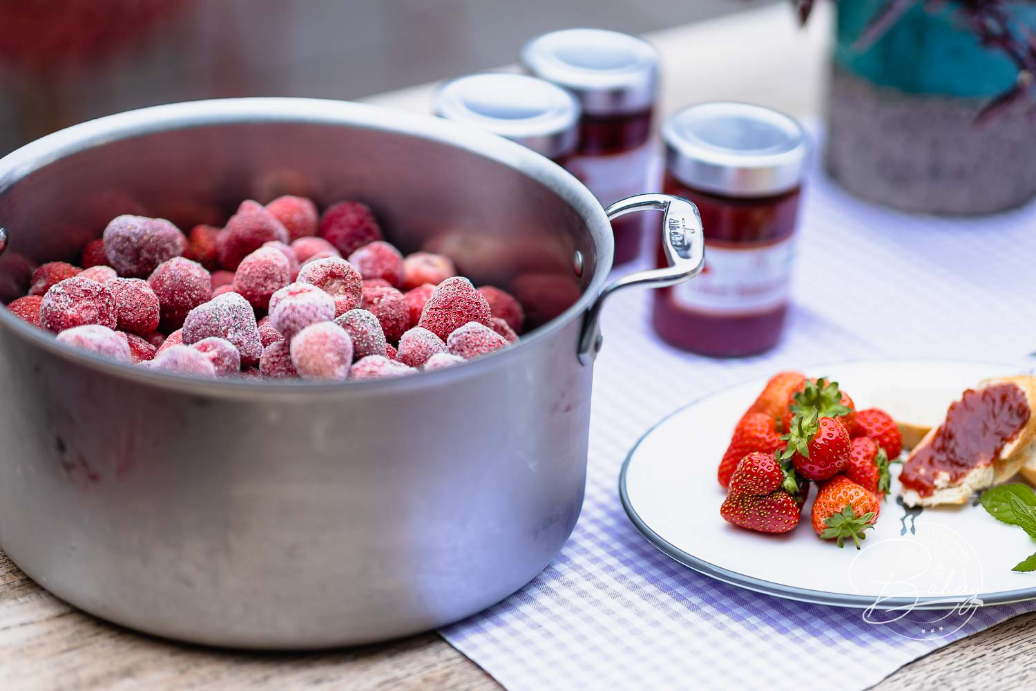 Großer Topf voller gefrorener Erdbeeren für die Erdbeermarmelade neben abgefüllten Gläsern