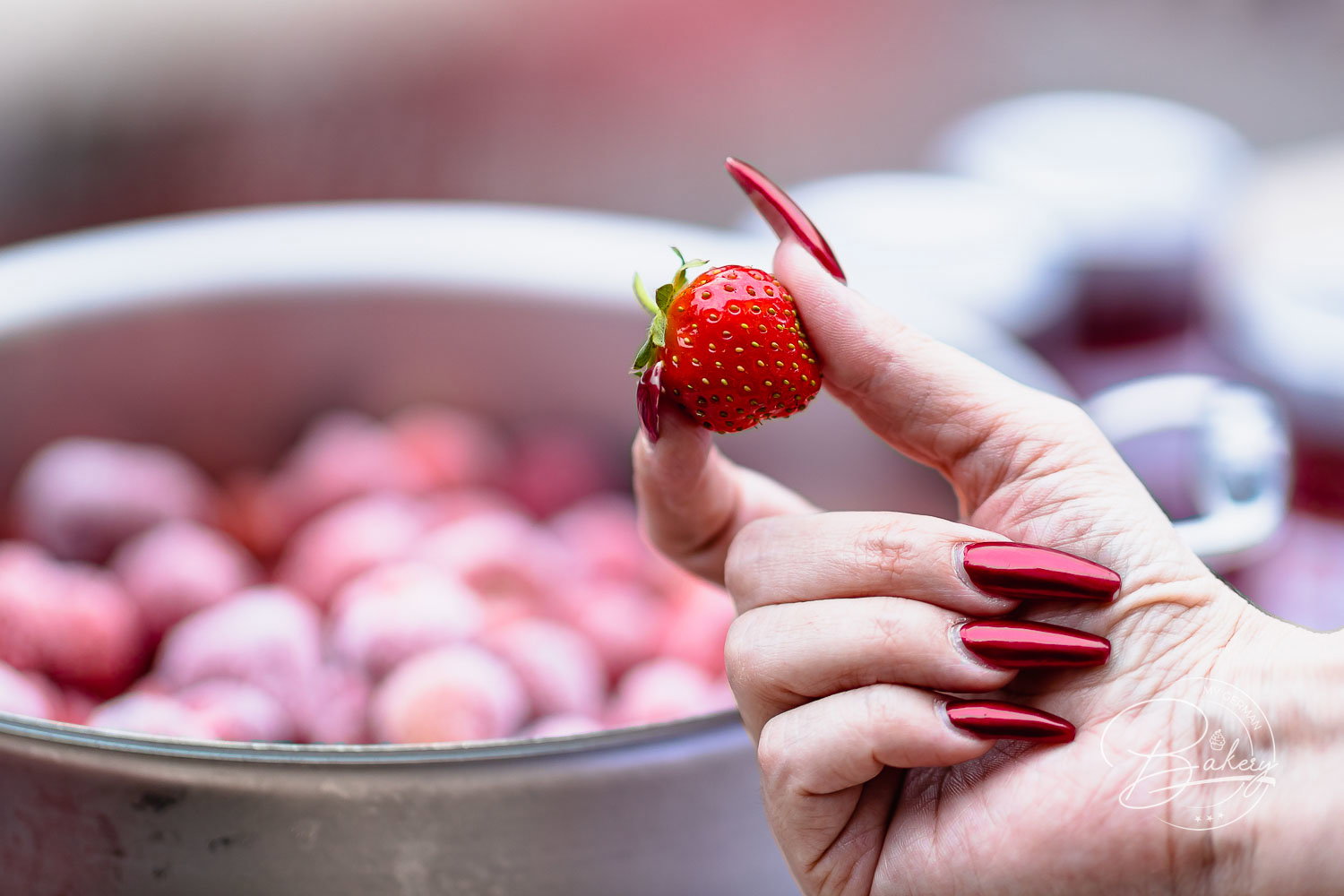 Hand hält eine frische Erdbeere über dem Topf mit gefrorenen Beeren für die Erdbeermarmelade
