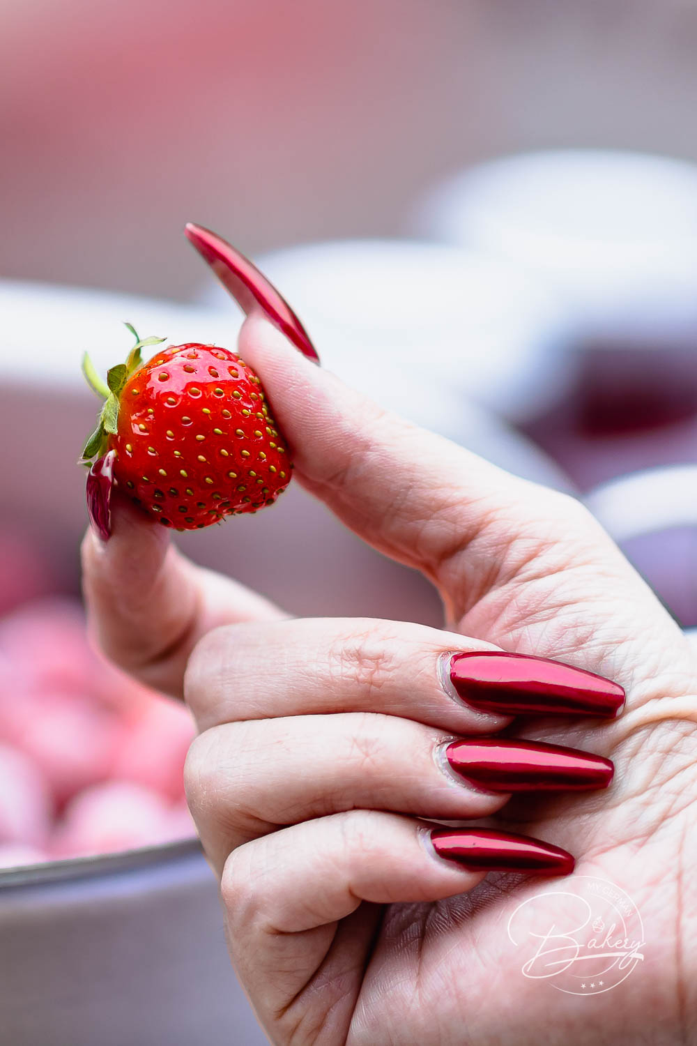Erdbeere zwischen den Fingern, im Hintergrund Gläser mit frisch gekochter Erdbeermarmelade