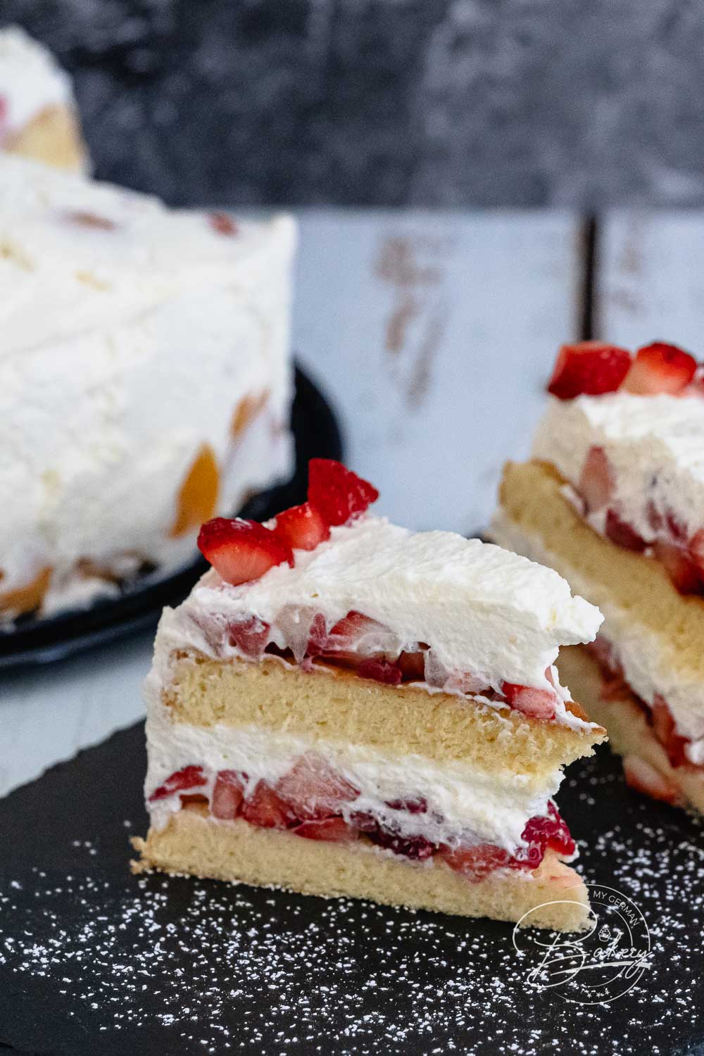 Nahaufnahme der geschichteten Erdbeer-Sahne-Torte mit Sahne und Erdbeerstücken zwischen Biskuitböden