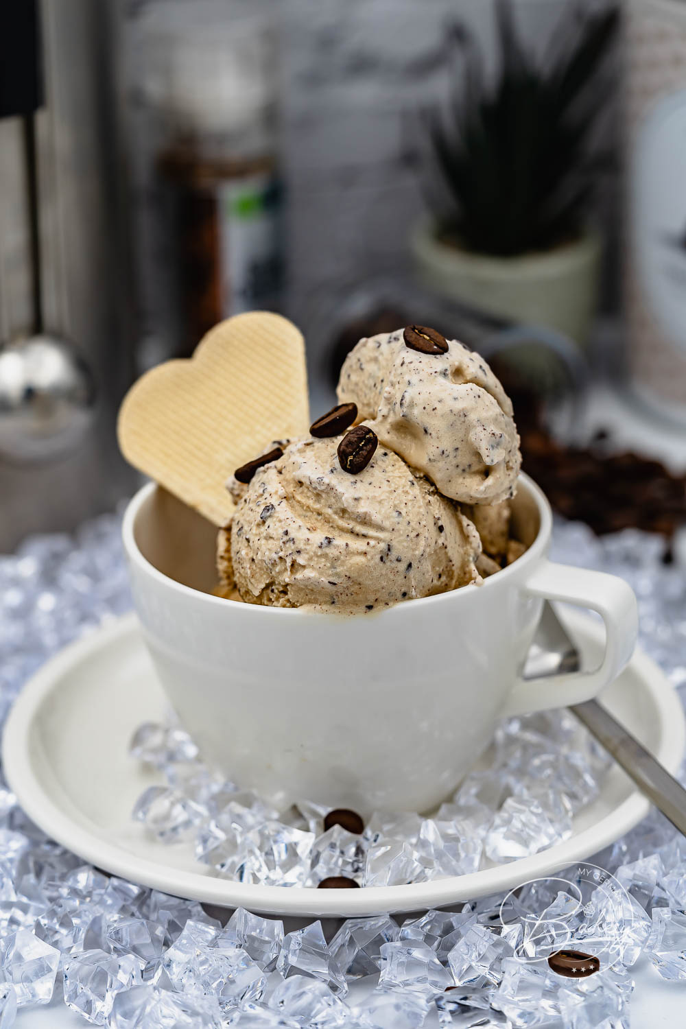 Kaffee Eis mit Schokostückchen in weißer Tasse, garniert mit Waffelherz und Kaffeebohnen