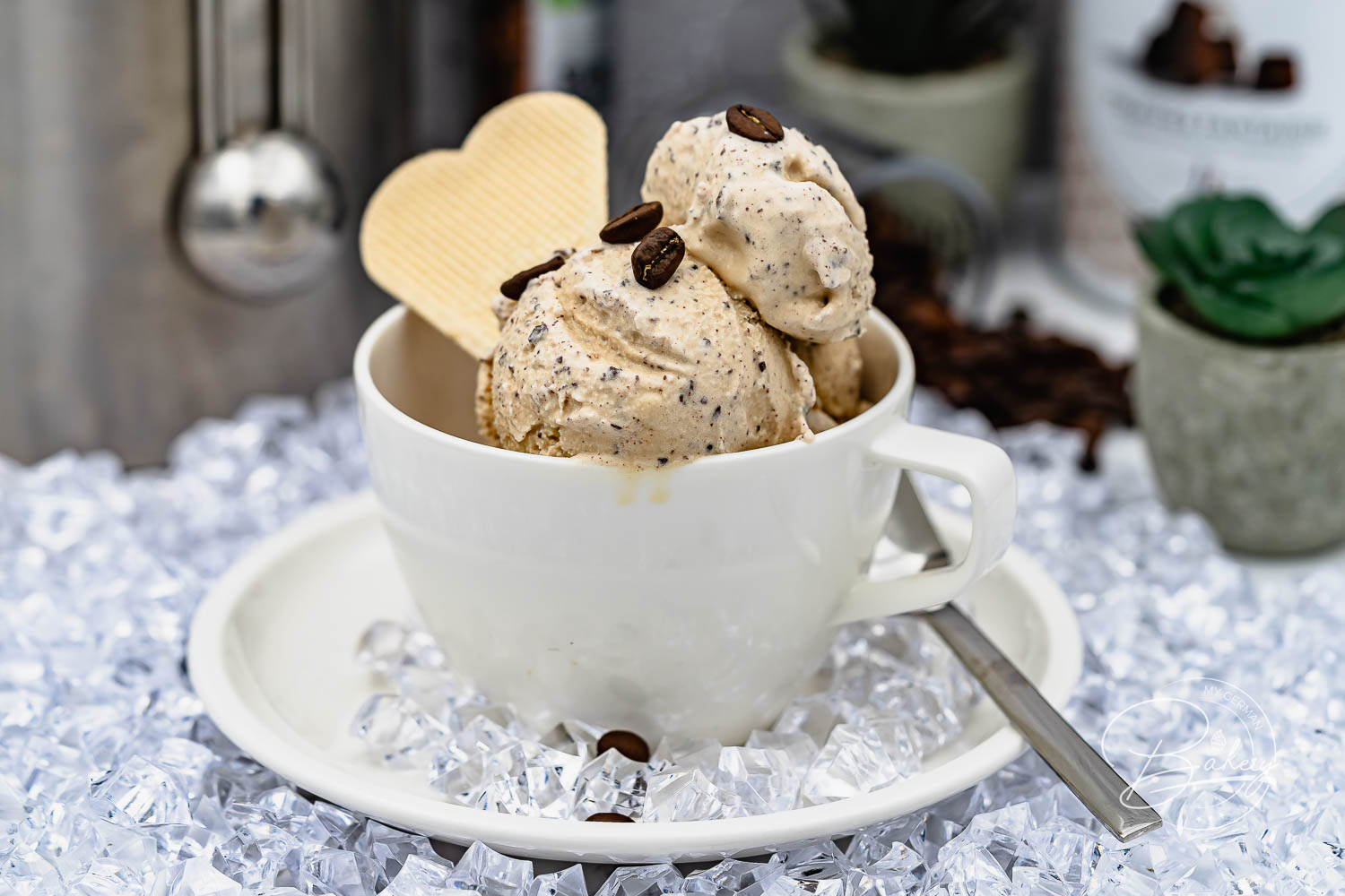 Zwei Kugeln cremiges Kaffee Eis in weißer Tasse mit Kaffeebohnen und Waffelherz