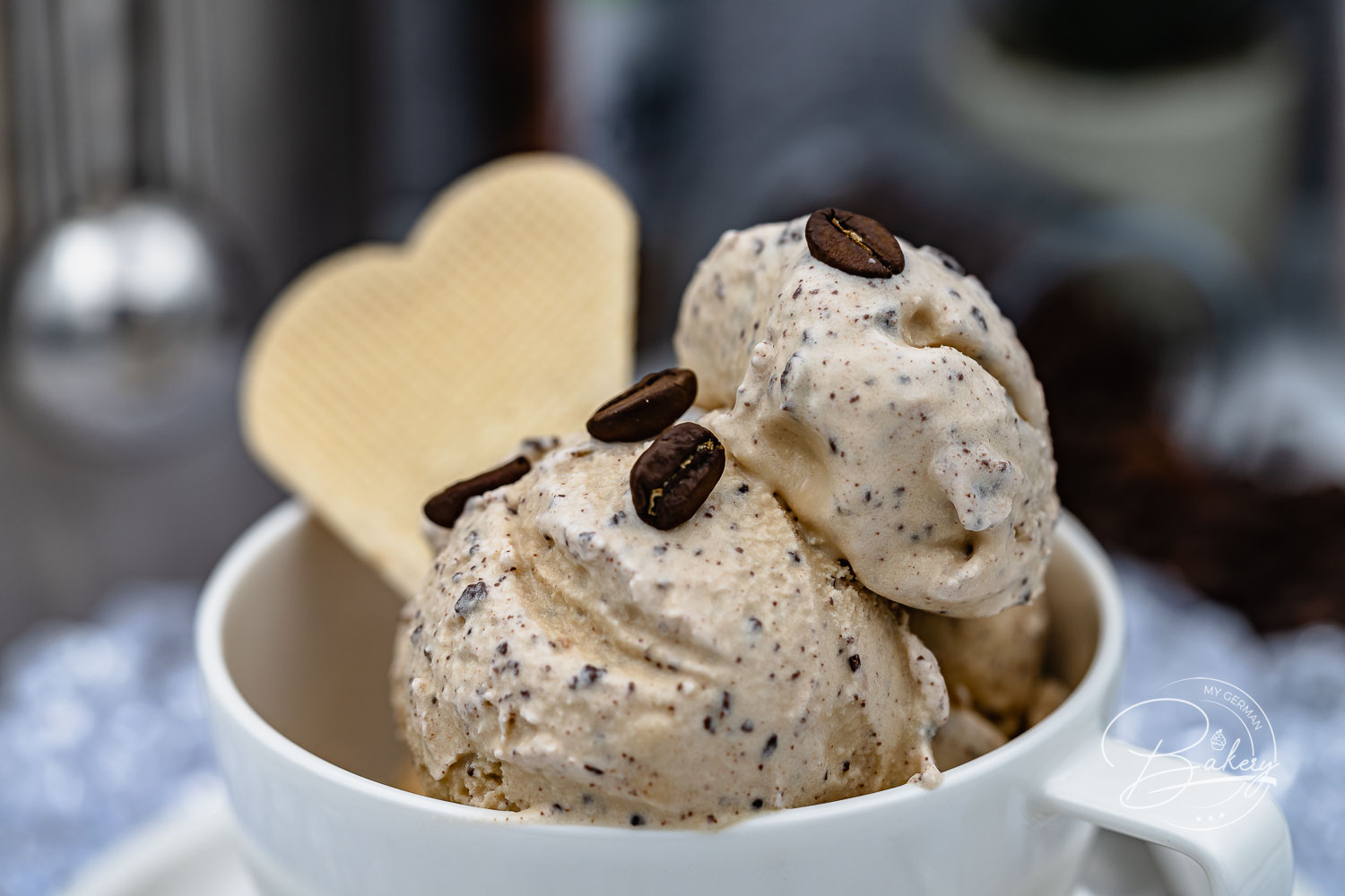 Nahaufnahme von cremigem Kaffee Eis mit Schokoladensplittern, Kaffeebohnen und Waffelherz