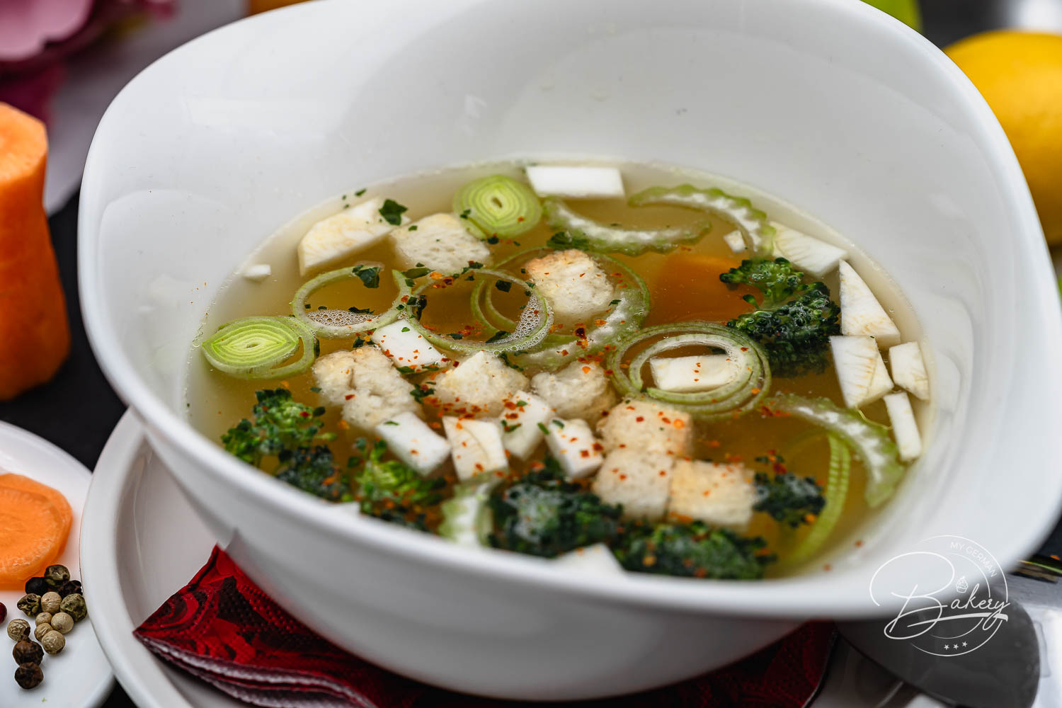 Nahaufnahme klassische Hühnersuppe mit Hähnchenwürfeln, Lauchringen, Brokkoli und Karotte in weißer Schale