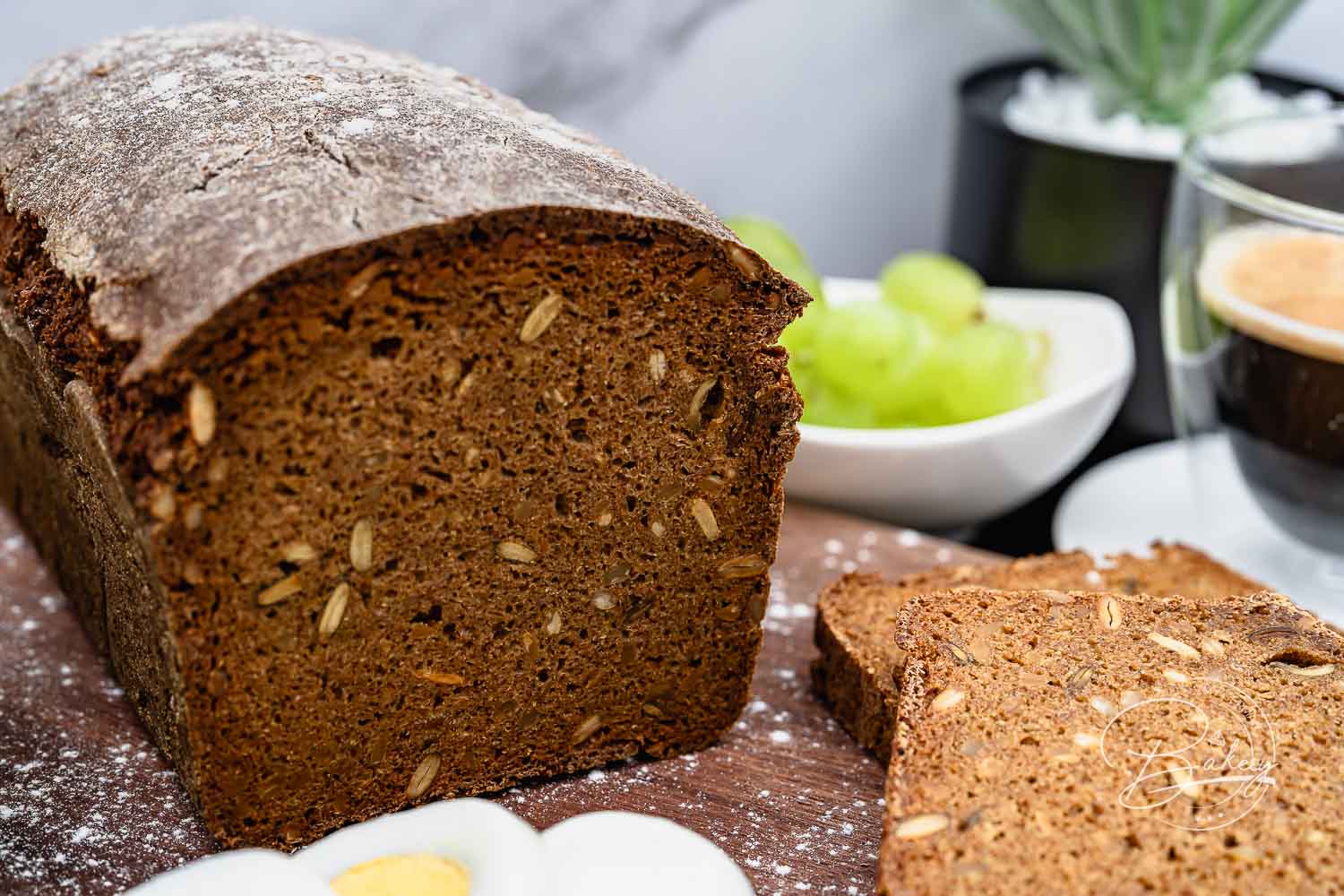 Angeschnittenes Vollkornbrot mit körniger Krume und Roggenschrot, Scheibe und Trauben daneben – Schwarzbrot Rezept