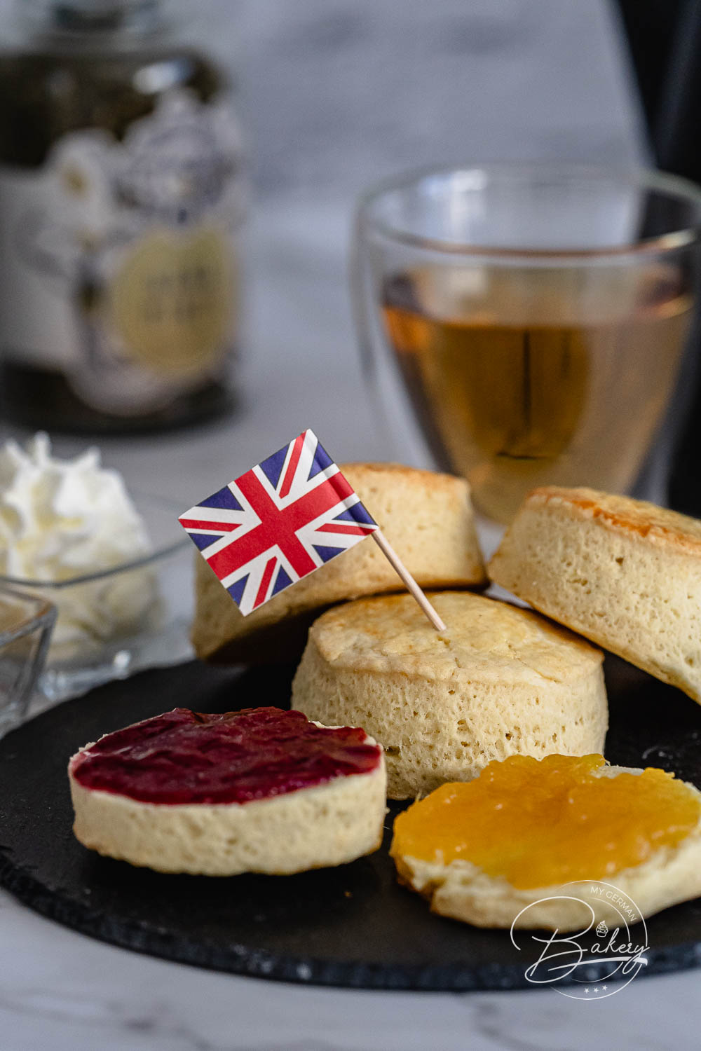 Halbierte Scones mit Erdbeer- und Orangenmarmelade bestrichen neben britischem Fähnchen