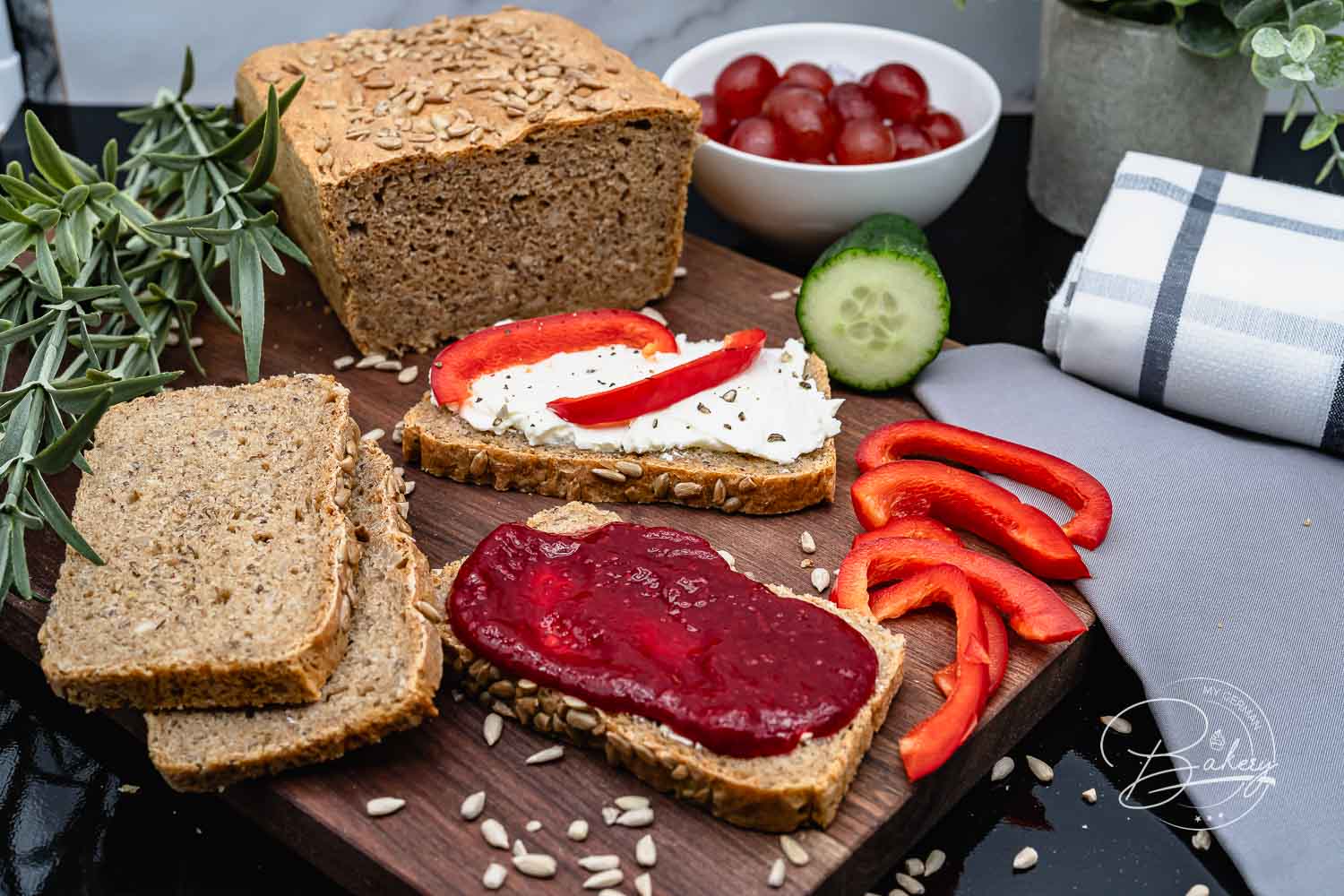 Dunkles Dinkel-Vollkornbrot mit Sonnenblumenkernen, dazu belegte Scheiben mit Frischkäse, Marmelade und Paprika