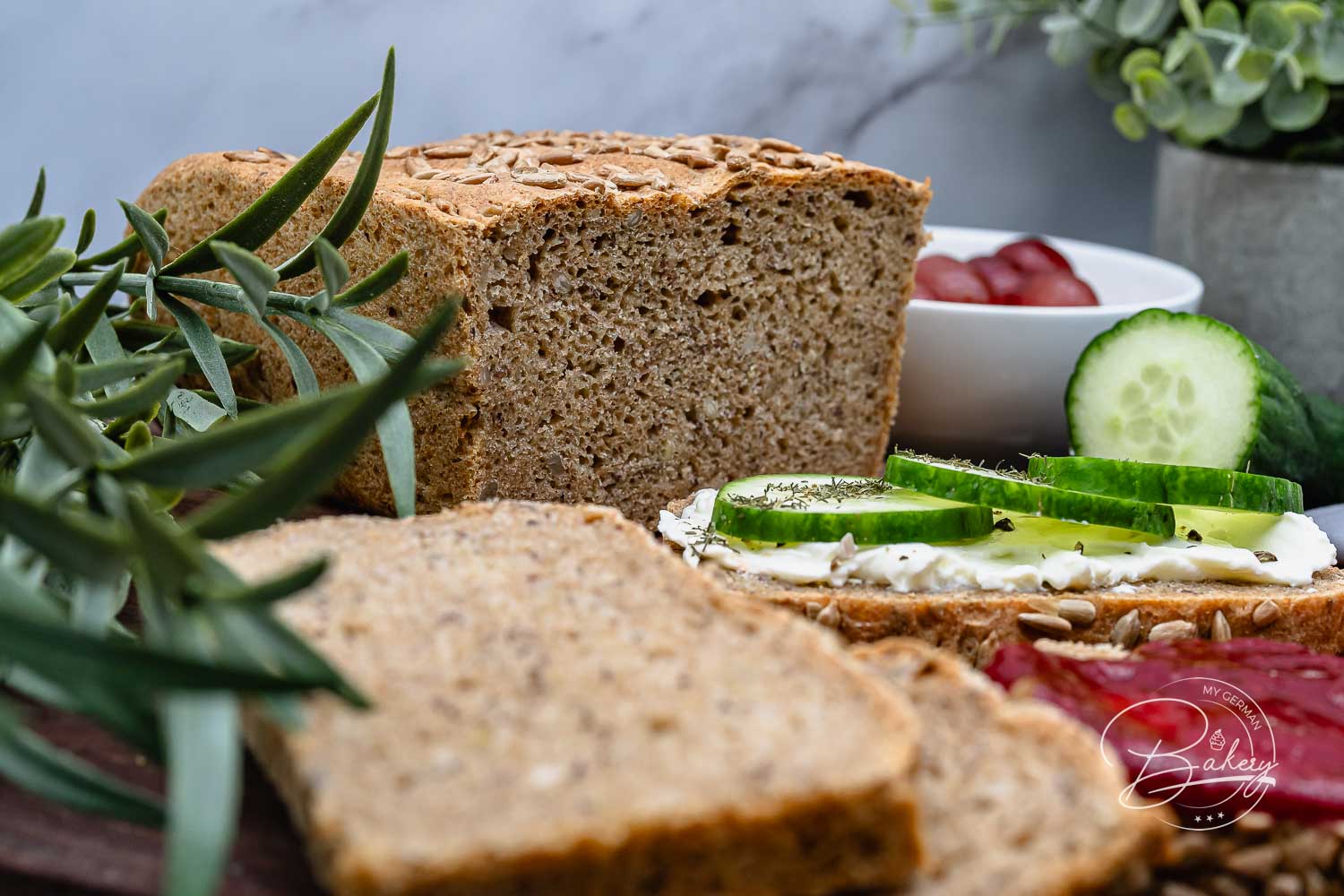 Nahaufnahme der Krume vom Dinkel-Vollkornbrot mit Saaten, daneben Rosmarin und belegte Scheibe