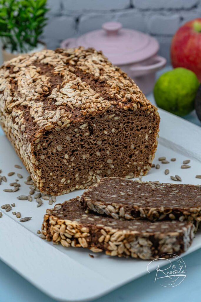 Aufgeschnittenes dunkles Vollkornbrot mit Kernen, daneben Scheiben auf weißem Teller