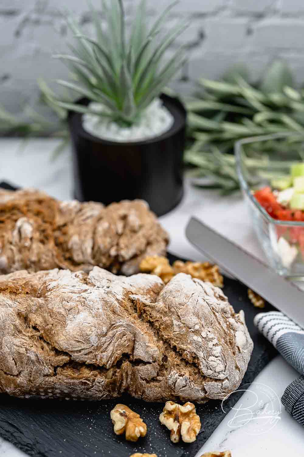 Längliches dunkles Vollkornbrot als Baguette geformt mit Walnüssen und Messer daneben
